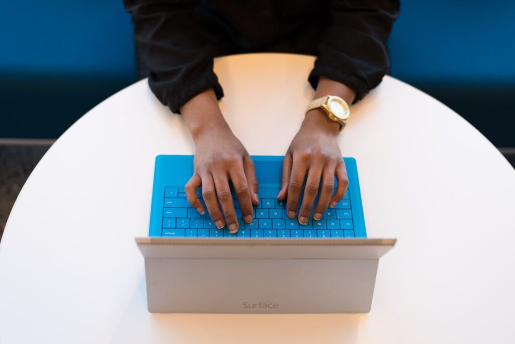 Hands of a person typing on a laptop with a blue keyboard, taken from above, ideal for technology themes.